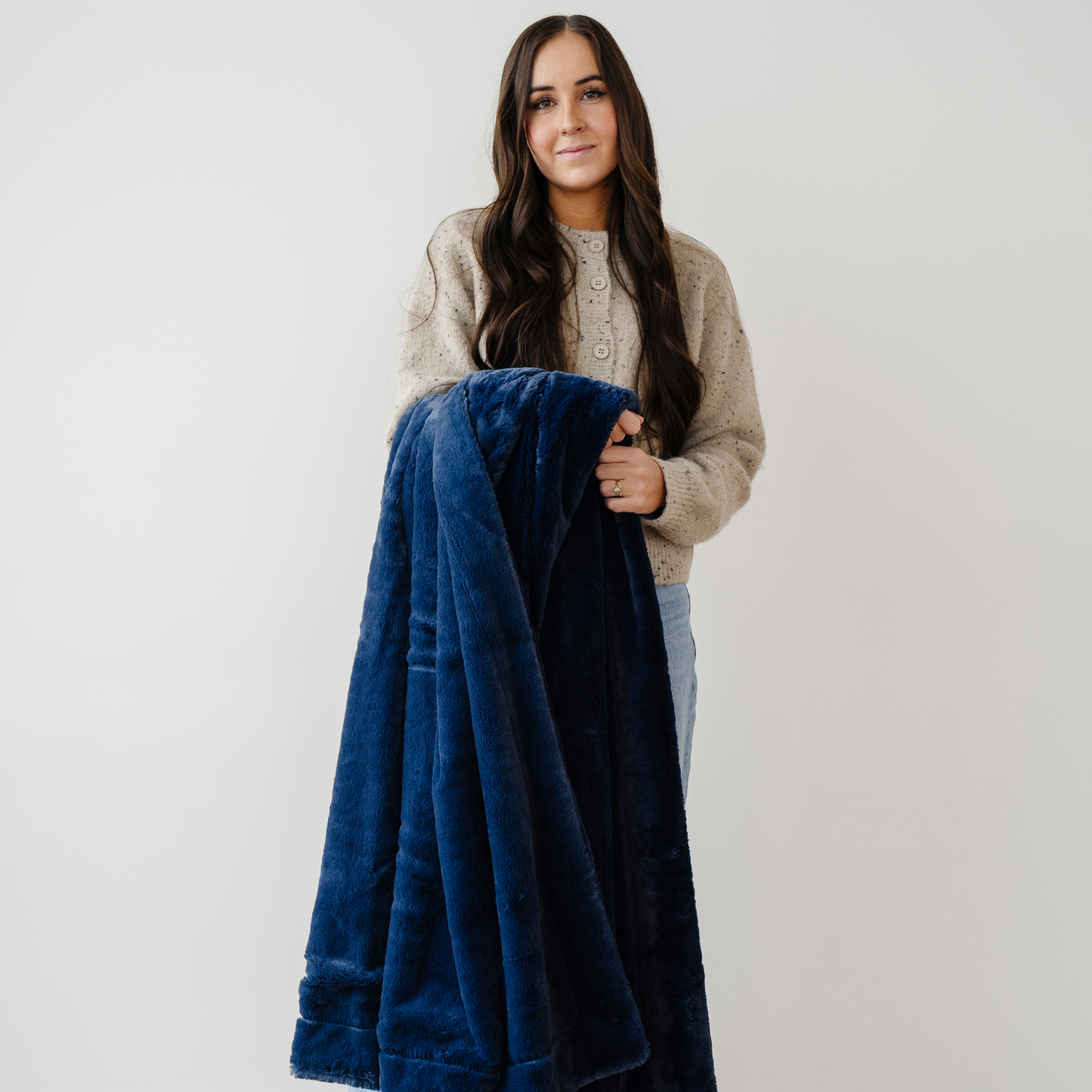 A woman holds a deep blue blanket that is a Saranoni blanket. This lush blanket is also a soft blanket and a luxury blanket. Use this cozy blanket for gifting, relaxing, or for home decor. Enjoy this extra large blanket for years to come. 