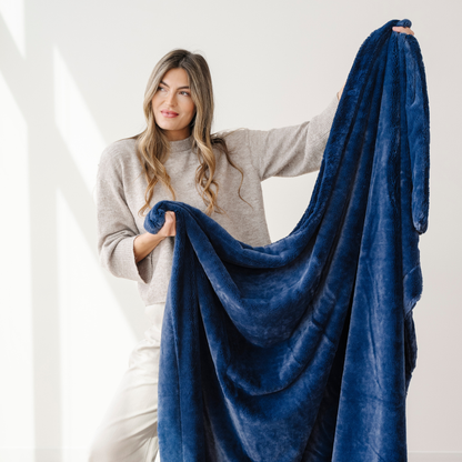 A woman holds up a deep blue blanket that is an extra large blanket. This soft blanket is a luxury blanket and a Saranoni blanket. Use this cozy blanket for gifting, relaxing, or as a home decor item. Enjoy this faux fur blanket for years to come!
