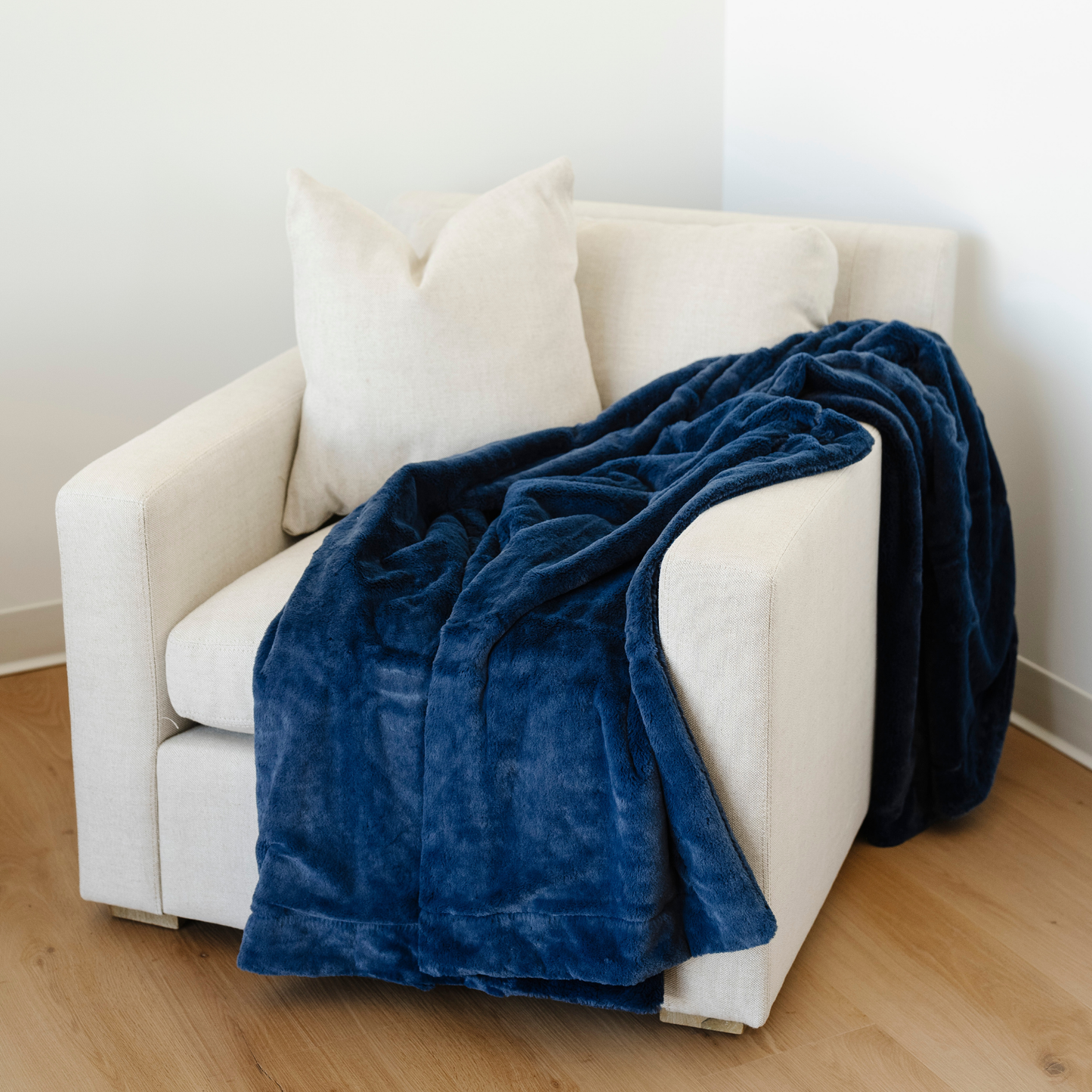 A beautiful deep blue blanket, that is a lush blanket, is draped on a chair. This soft blanket is a luxury blanket and a Saranoni blanket. Use this gorgeous blanket for relaxing, gifting, or as a home decor item. Embrace luxury that lasts with this cozy blanket.