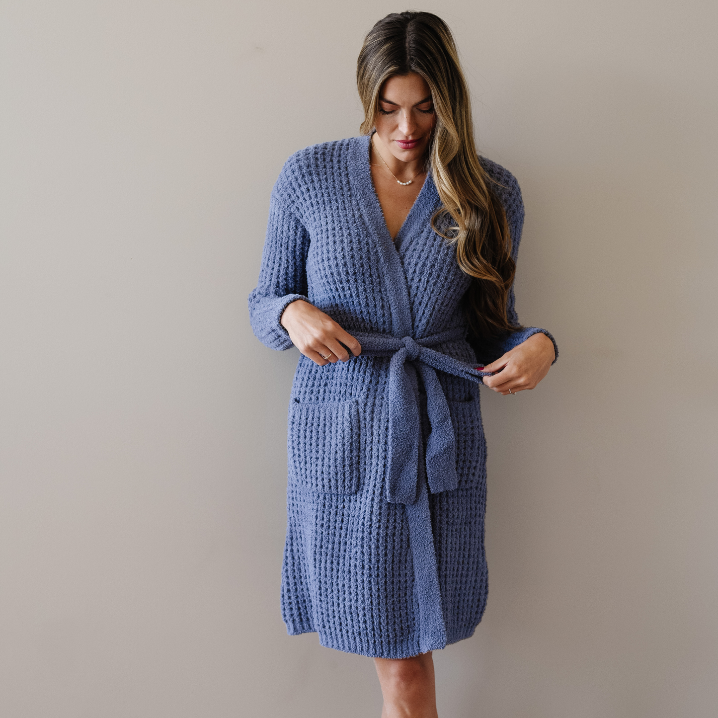 Woman stands wearing an oxford blue waffle knit robe. 