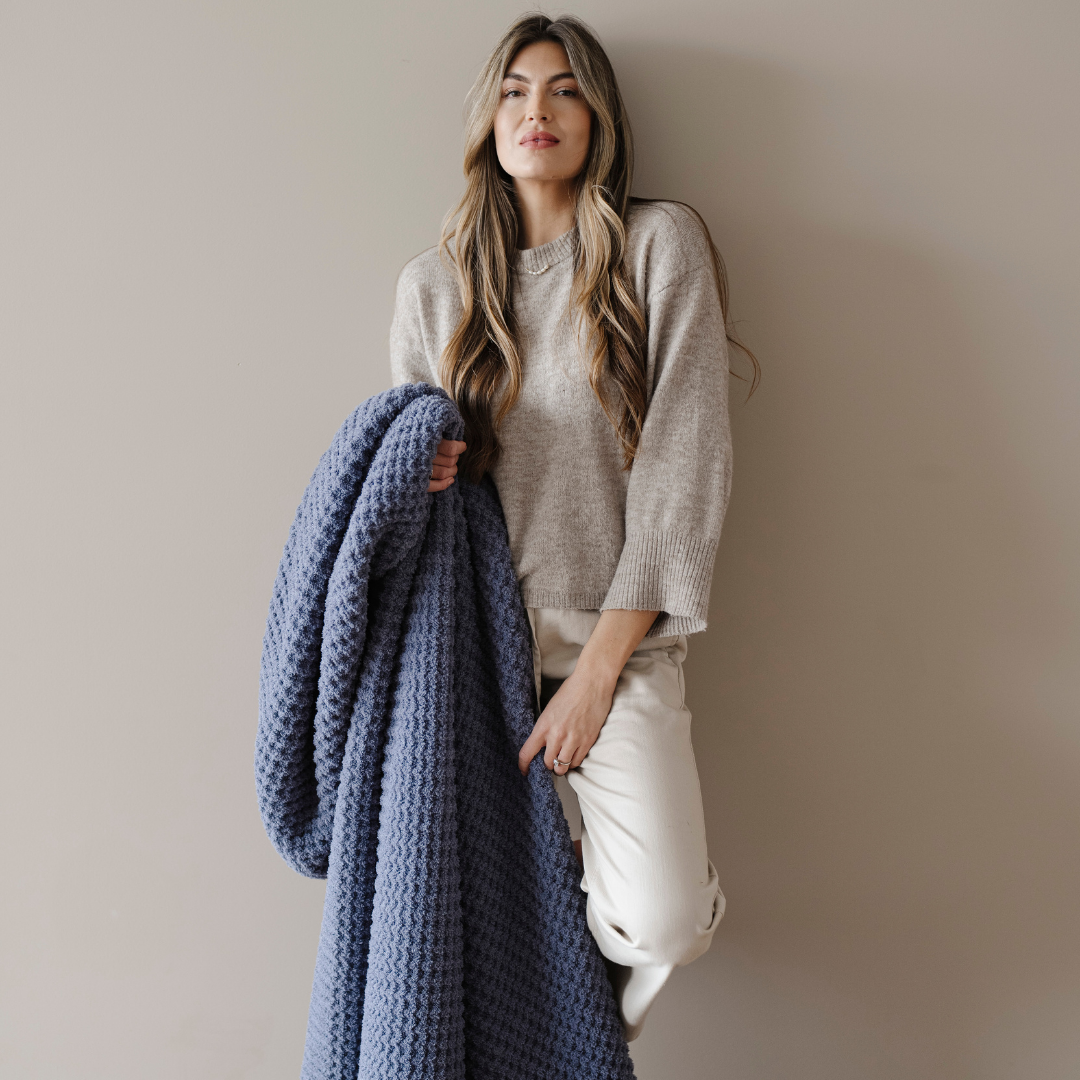 A woman holds a blue waffle knit blanket that is an extra large blanket. This soft blanket is very stretchy and breathable and is also a very cozy blanket. Enjoy this Saranoni blanket for years to come!