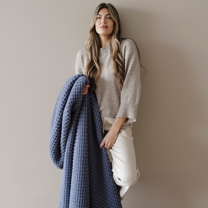 A woman holds a blue waffle knit blanket that is an extra large blanket. This soft blanket is very stretchy and breathable and is also a very cozy blanket. Enjoy this Saranoni blanket for years to come!