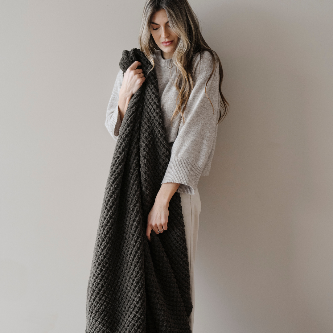 A woman holds a green blanket that is a waffle knit blanket. This soft blanket is a Saranoni blanket and is great for relaxing, gifting, or as home decor. Enjoy this cozy extra large throw blanket for  years.