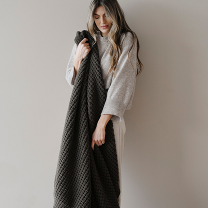 A woman holds a green blanket that is a waffle knit blanket. This soft blanket is a Saranoni blanket and is great for relaxing, gifting, or as home decor. Enjoy this cozy extra large throw blanket for  years.