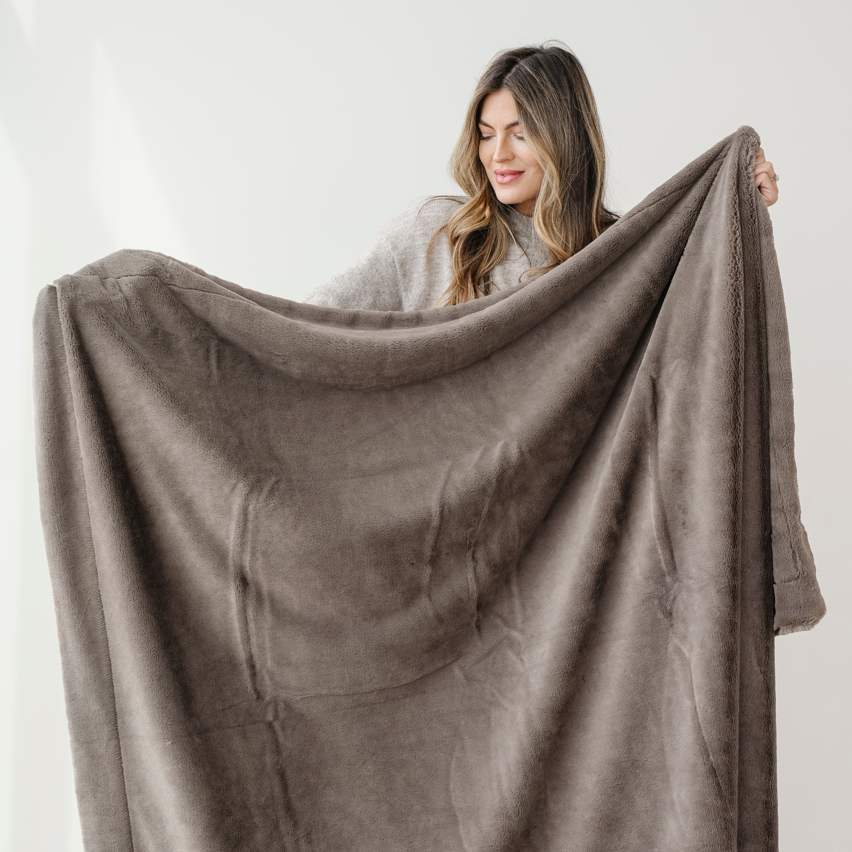 A woman holds a brown lush Saranoni blanket. This soft blanket is a luxury blanket and a Saranoni blanket. This cozy blanket is a great home decor staple and is also perfect for gifting or relaxing with. Enjoy this faux fur blanket for years to come!