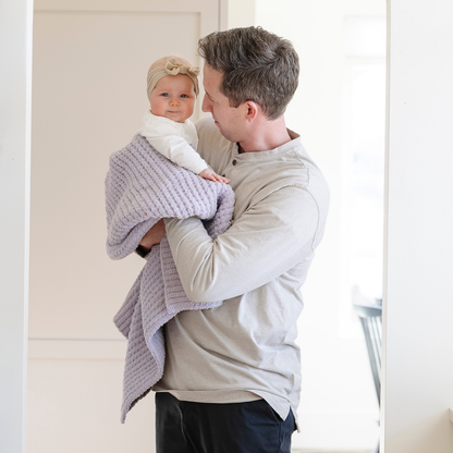 A father holds his little girl in a buttery-soft Saranoni blanket, featuring a breathable, plush waffle texture in a soothing light purple hue. This luxury receiving blanket is the best baby blanket as a  newborn blanket, infant blanket, baby blanket, or toddler blanket—perfect as a cozy blanket for snuggles or a must-have infant blanket. Designed for softness and comfort, this plush baby blanket makes an ideal baby gift or gift for new moms. Enjoy this luxury blanket!