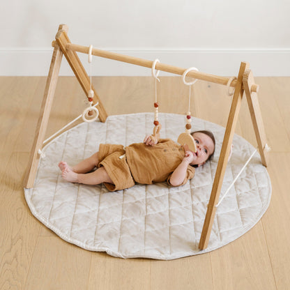 A little boy lays on a soft moonbeam colored minky play mat in a circle shape, 36 inches in diameter, with durable quilting. Ideal as a portable and quilted baby play mat for on-the-go comfort and easy packing in a diaper bag.