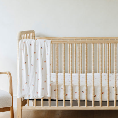 A Minky Stretch Luxe swaddle in a apple pattern, featuring ultra-soft minky fabric with a luxurious stretch, perfect for keeping your baby cozy and comfortable. Ideal for newborns and infants is on a crib where the Minky Stretch Luxe crib sheet in a apple pattern, designed with soft and stretchy minky fabric for ultimate comfort. Perfect fit for standard crib mattresses, offering a cozy and luxurious sleep environment for your baby is on the crib mattress.