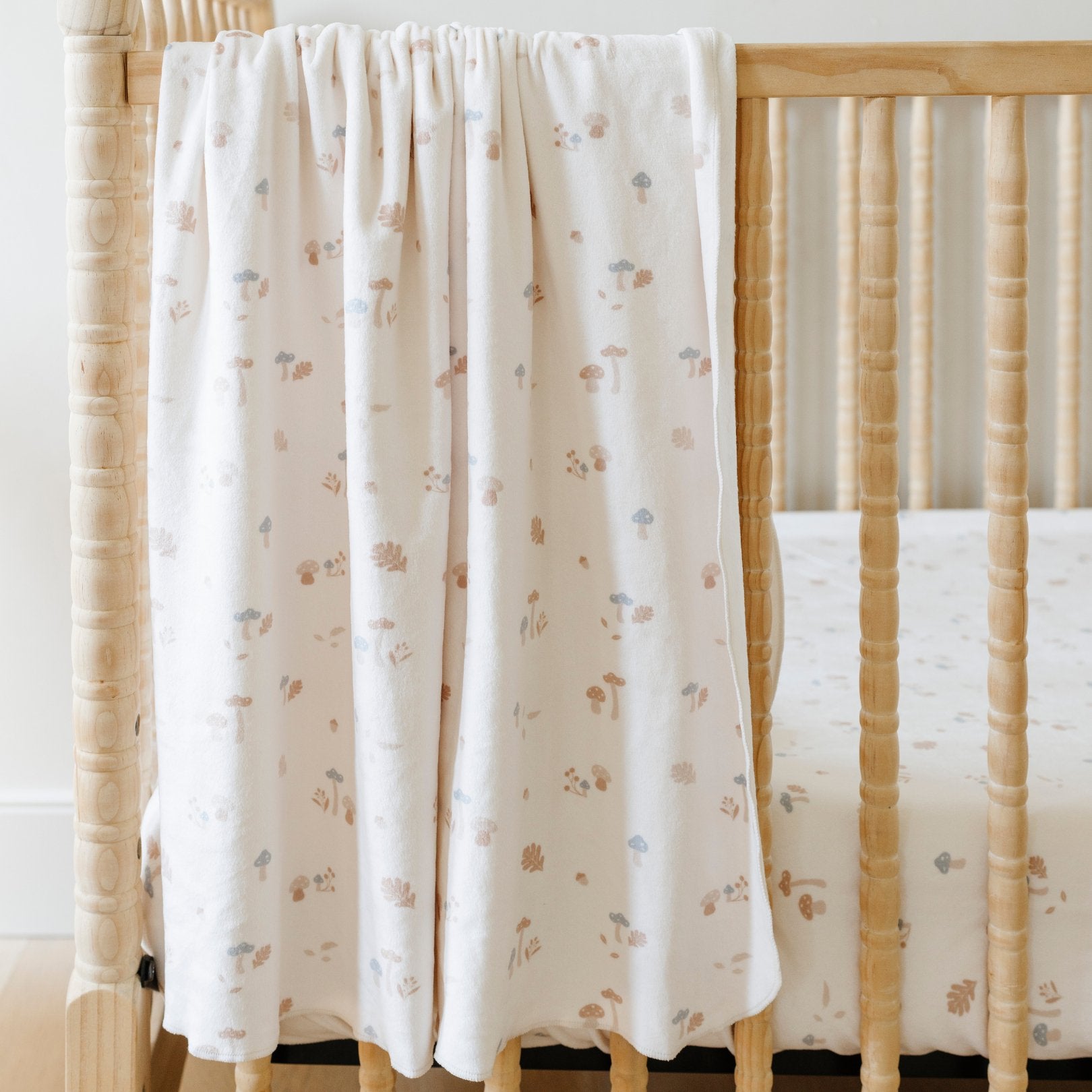 A Minky Stretch Luxe swaddle in a mushroom pattern, featuring ultra-soft minky fabric with a luxurious stretch, perfect for keeping your baby cozy and comfortable. Ideal for newborns and infants is on a crib where the Minky Stretch Luxe crib sheet in a mushroom pattern, designed with soft and stretchy minky fabric for ultimate comfort. Perfect fit for standard crib mattresses, offering a cozy and luxurious sleep environment for your baby.