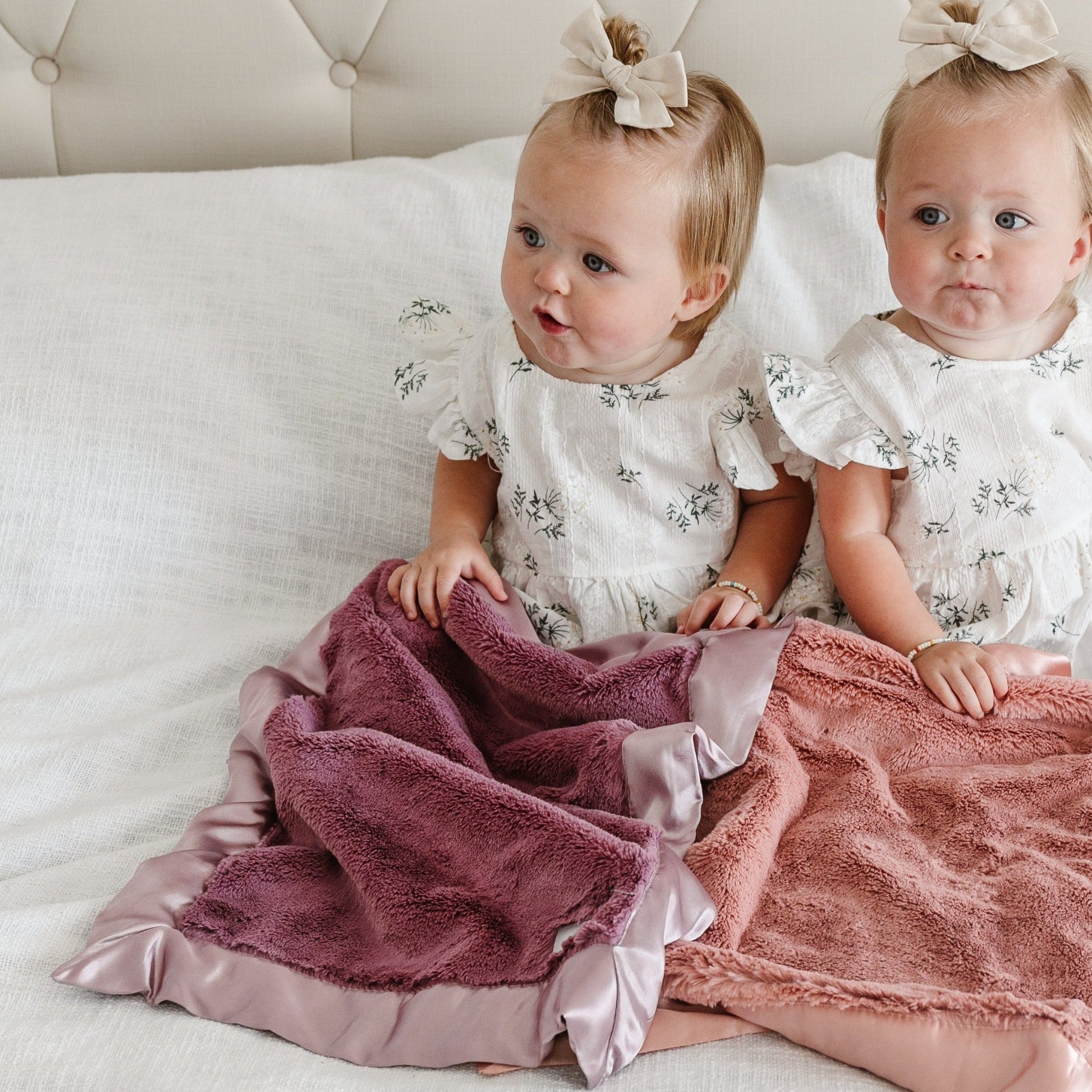 Two sisters snuggle under cute satin bordered mini blankets.