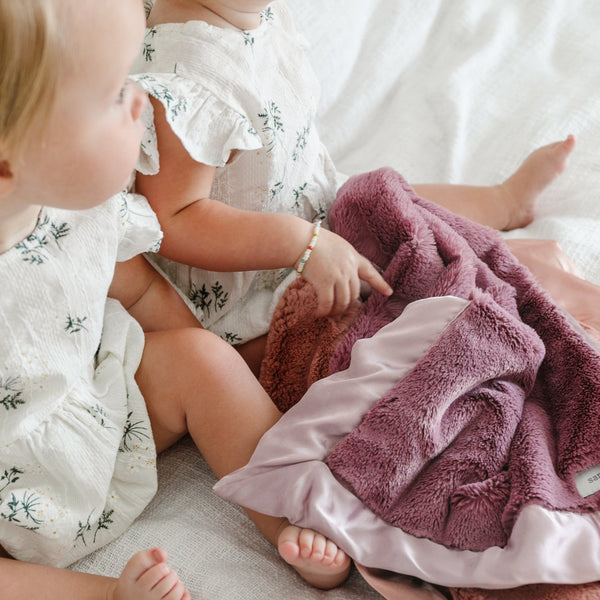 Mauve@Two babies lay with a beautiful dusty purple colored satin blanket.