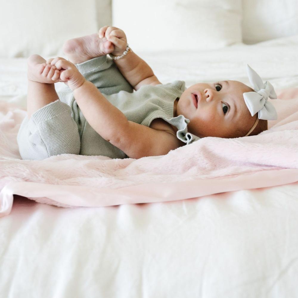 Baby snuggling and enjoying a light pink satin bordered mini blanket.