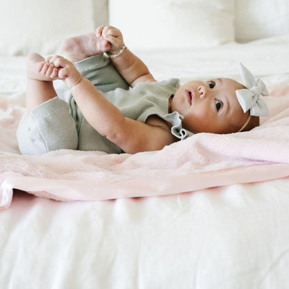 Baby snuggling and enjoying a light pink satin bordered mini blanket.
