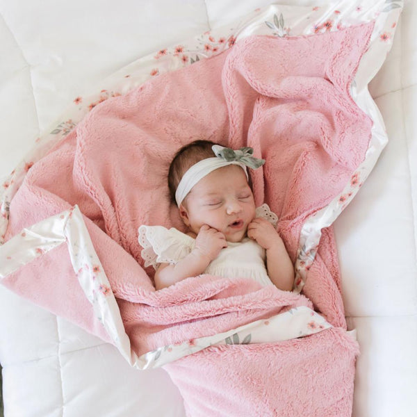 Newborn wrapped in cozy pink satin floral baby blanket.