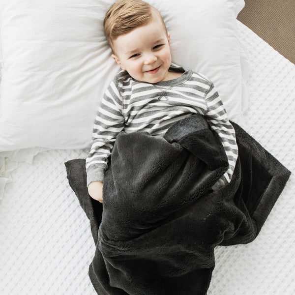 Young boy on white bed with dark gray baby blanket