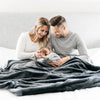 Parents admiring baby underneath a gorgeous oversized charcoal throw blanket.