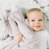 A smiling baby holds their warm security blanket close to their face.