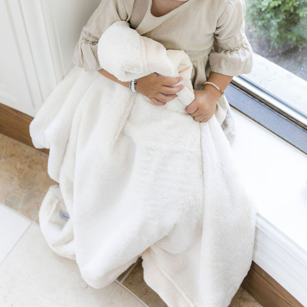 Little girl hugging ivory baby blanket in a window