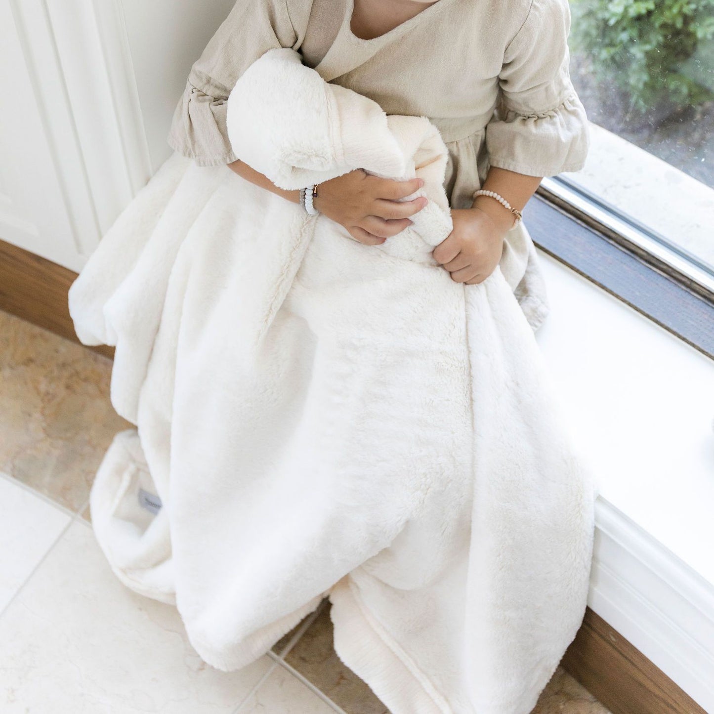A little girl holds a Luxury Receiving Natural (off-white) Colored Lush Saranoni Blanket. The soft blanket is a small blanket and a baby blanket or toddler blanket.