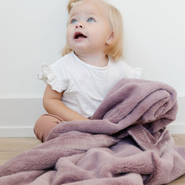 A cute girl snuggles up in her dusty pink blanket for babies and toddlers.