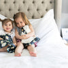 Two cute girls sit on the bed with their ivory floral plush baby blankets.