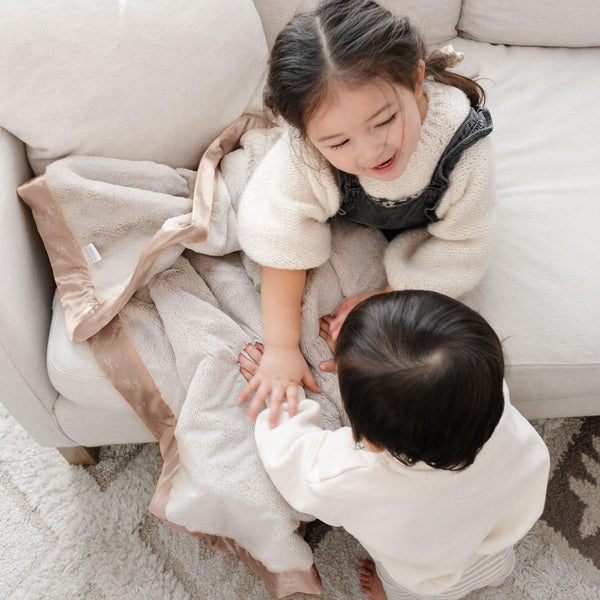Two siblings playing with each other hold a super comfy Saranoni blanket.