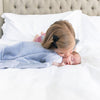 A little girl kisses an adorable baby that is snuggled up in a gorgeous Saranoni baby blanket.