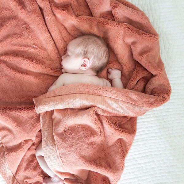 A baby laying on its stomach sleeps in a beautiful kids blanket.