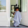 A little boy carries his silky soft lush blanket with him as he walks out the door.
