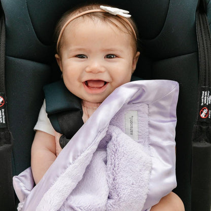 Light purple mini blanket with a velvety surface and a sleek satin border, designed to combine warmth with a sophisticated, silky finish.