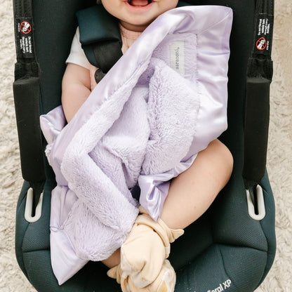 Detailed shot showing the warm and inviting textures of a light purple mini satin bordered blanket. 