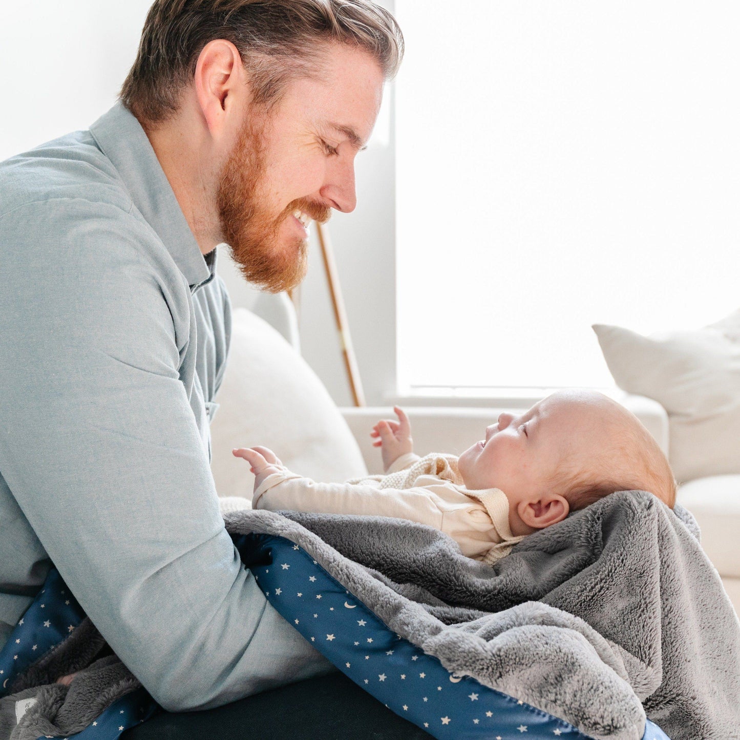 Father and child bonding together while baby is wrapped in a cozy star satin border blanket. 
