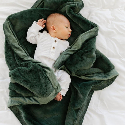 A little baby lays in a Luxury Receiving Hunter Green Colored Lush Saranoni Blanket. The soft blanket is a small blanket and a baby blanket or toddler blanket.