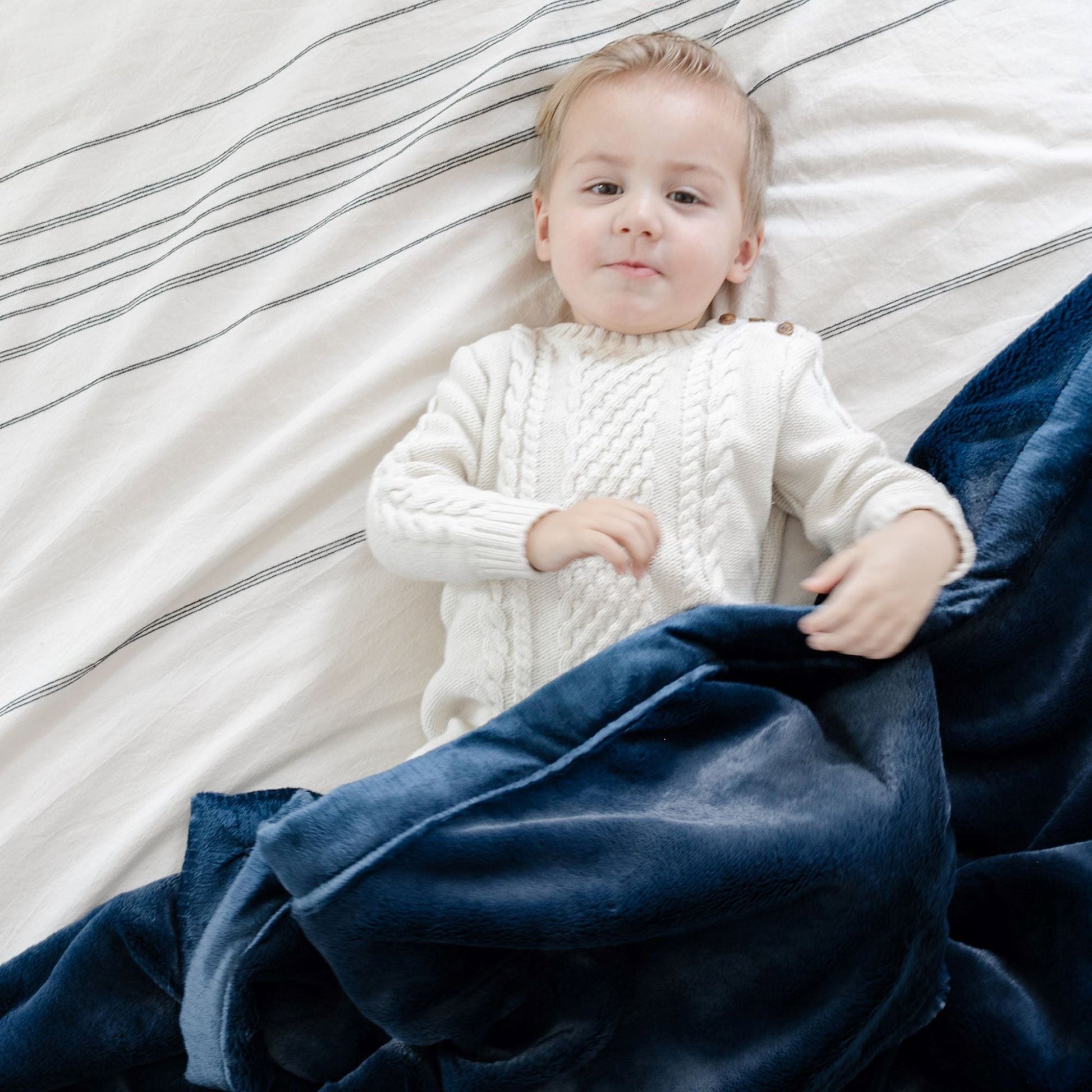 A little boy lays under a Luxury Receiving Navy Colored Lush Saranoni Blanket. The soft blanket is a small blanket and a baby blanket or toddler blanket.