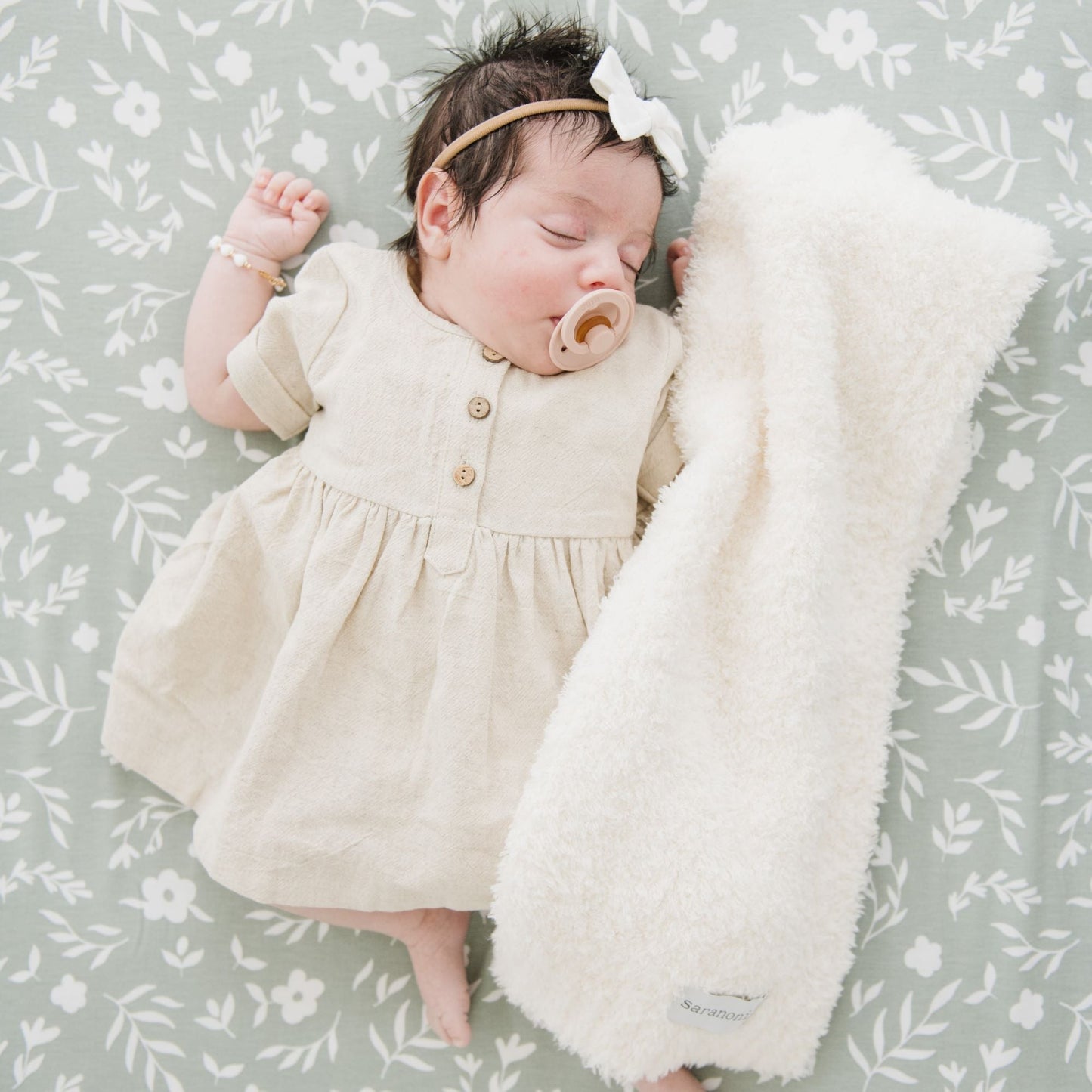 Baby girl sleeping on stretchy crib sheets with white BAMBONI MINI BLANKETS - Saranoni