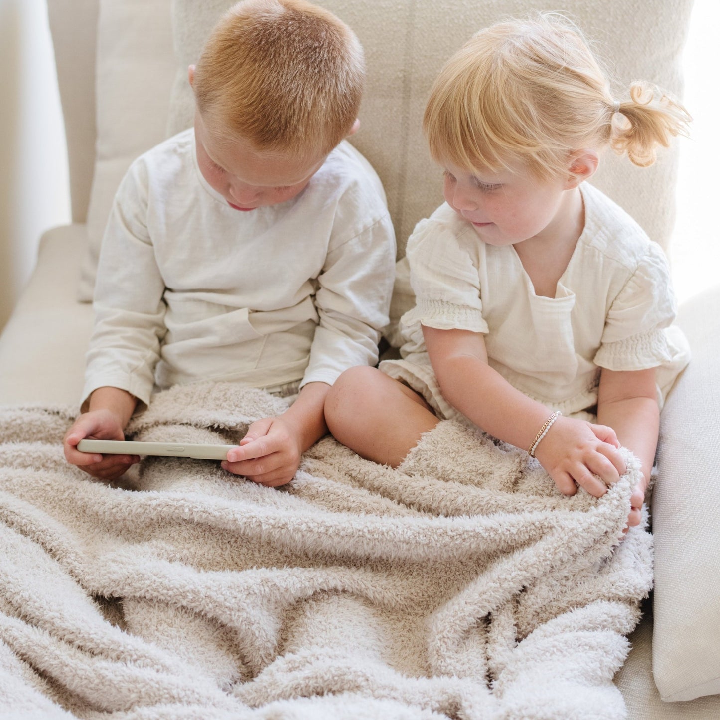 Two adorable little kids sitting on chair with Buttermilk BAMBONI® TODDLER BLANKETS - Saranoni