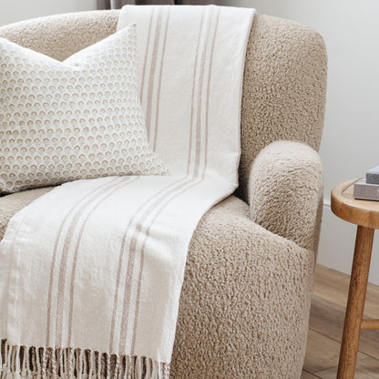 Close-up of white xl throw blanket with beige stripes draped over beige armchair- Saranoni
