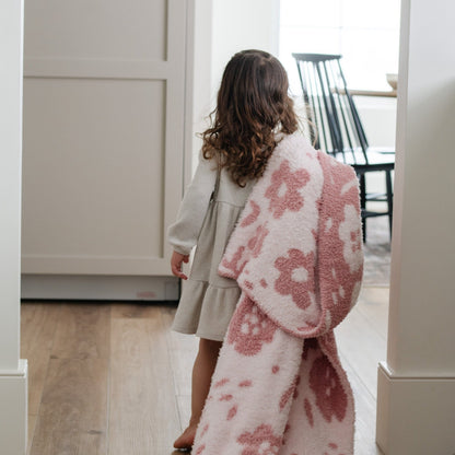 A little girl holds a double-layer Bamboni® blanket. The plush, breathable blanket features a two-tone light pink and pink floral design, offering ultimate softness and warmth. Made from Saranoni’s signature stretchy, cloud-like Bamboni® fabric, this luxury kids blanket provides comfort for naps and on-the-go snuggles. The soft blanket is a toddler blanket and Saranoni blanket. 