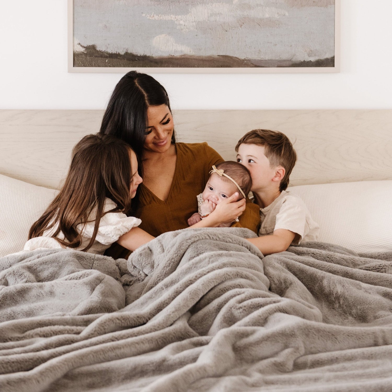 A mother and her children share warm moments under a Saranoni Grand Faux Fur blanket, featuring an elegant gray tone and luxuriously soft texture. This cozy, queen-sized blanket and faux fur blanket offers soothing weight, premium softness, timeless comfort, and is a soft blanket. Perfect as a big blanket and luxury blanket for snuggling or as a luxury bedroom accent, this Saranoni blanket elevates every cozy moment and is a cozy blanket.