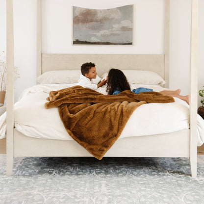 A little boy and his sister are on a bed with a Saranoni Grand Faux Fur blanket, featuring an elegant golden tone and luxuriously soft texture. This cozy, throw blanket and faux fur blanket offers soothing weight, premium softness, timeless comfort, and is a soft blanket. Perfect as a cozy blanket and luxury blanket for snuggling or as a luxury bedroom accent, this Saranoni blanket elevates every cozy moment and is a cozy blanket.